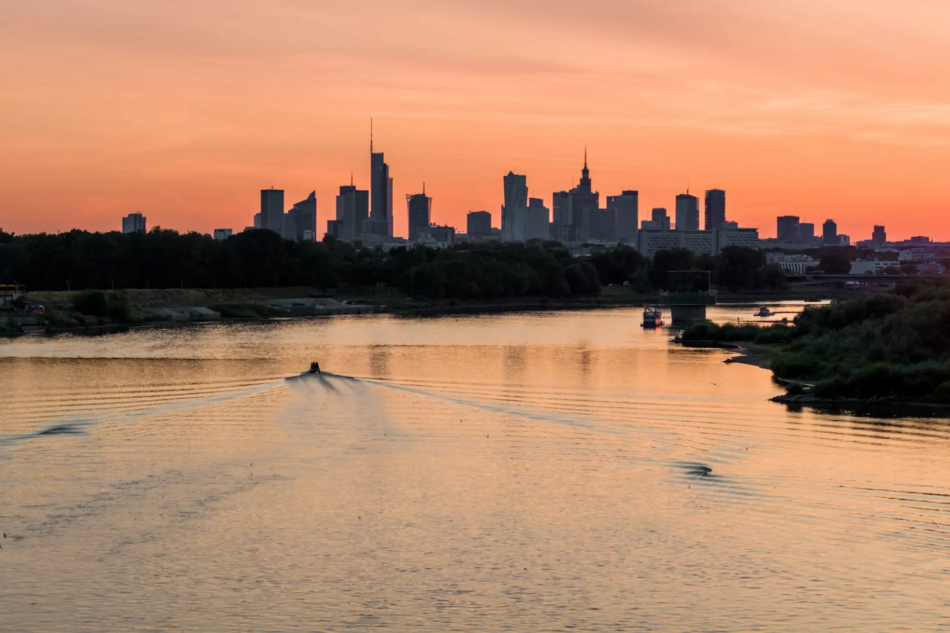 A boat traveling down a river with a city skyline in the background